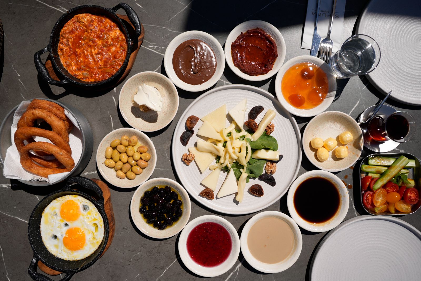 Yukarıdan çekilmiş zengin Türk kahvaltısı sofrası; menemen, peynir tabağı, zeytin, reçeller ve çay